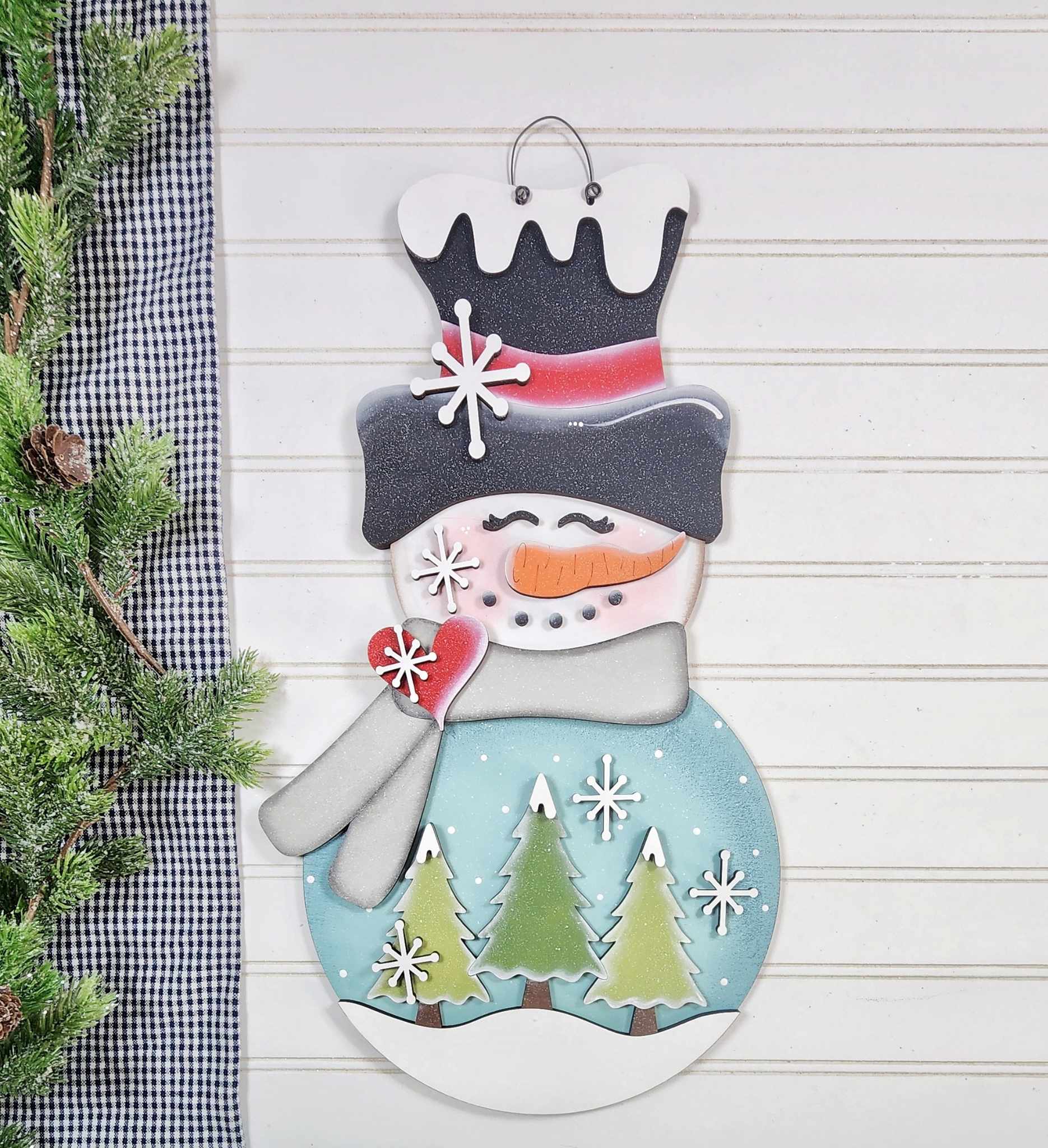 Decorative snowman ornament with a checkered cloth and greenery in the background