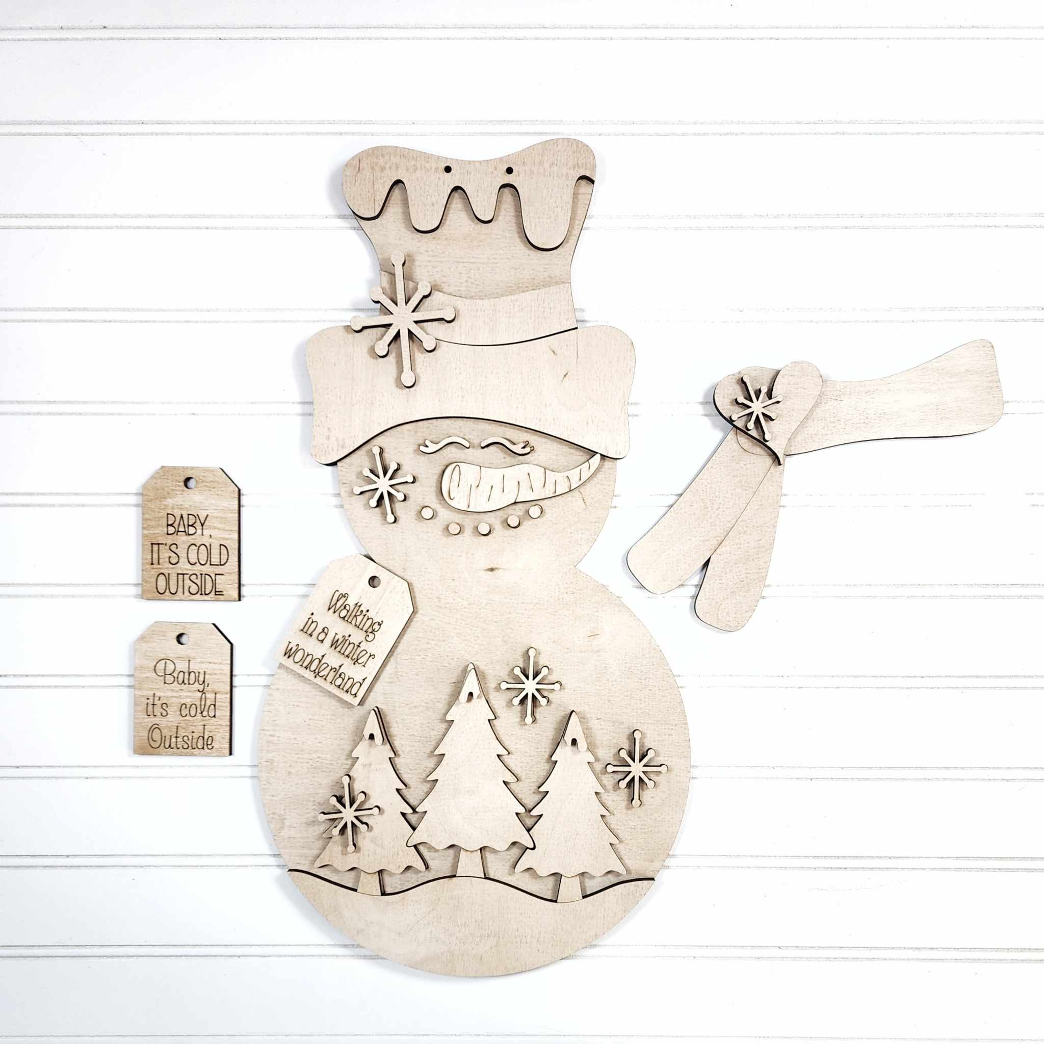 Wooden snowman ornament with engraved trees and text on a white background