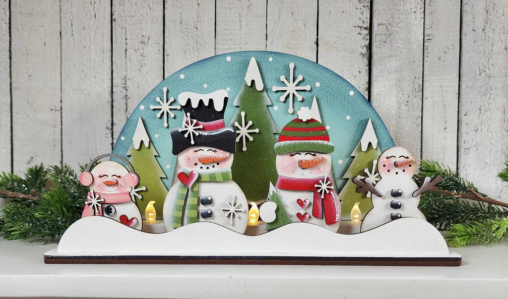Decorative wooden panel with snowmen and a snowflake design against a wooden background.
