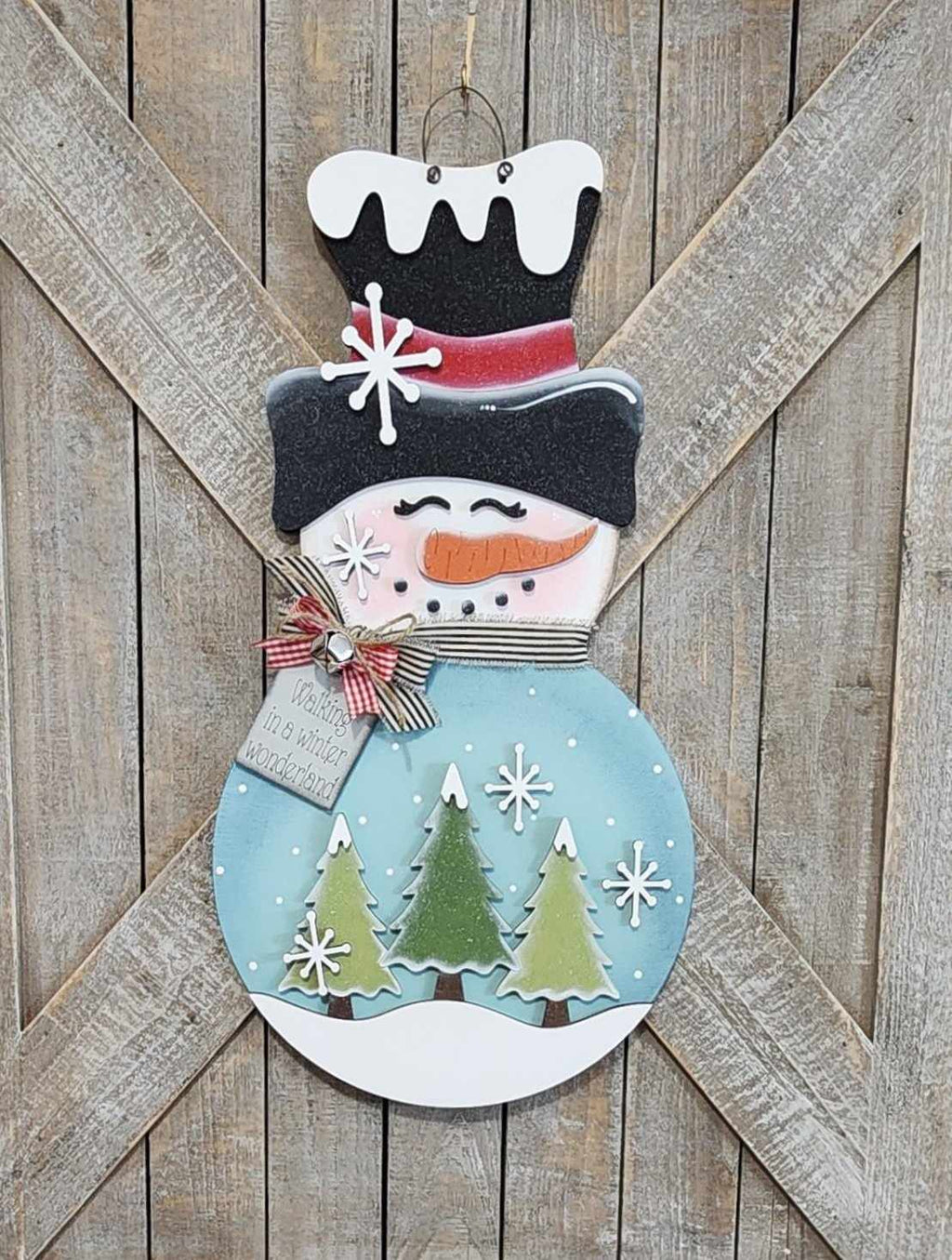 Decorative snowman door hanger with trees on a wooden background