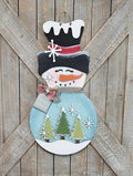 Decorative snowman door hanger with trees on a wooden background