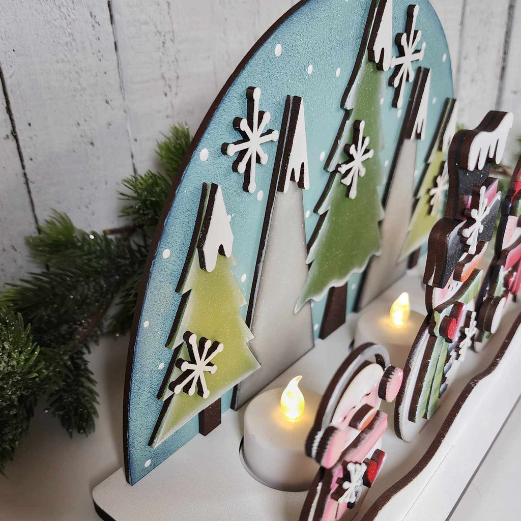 Decorative wooden scene with trees and people around a lit candle on a white wooden background