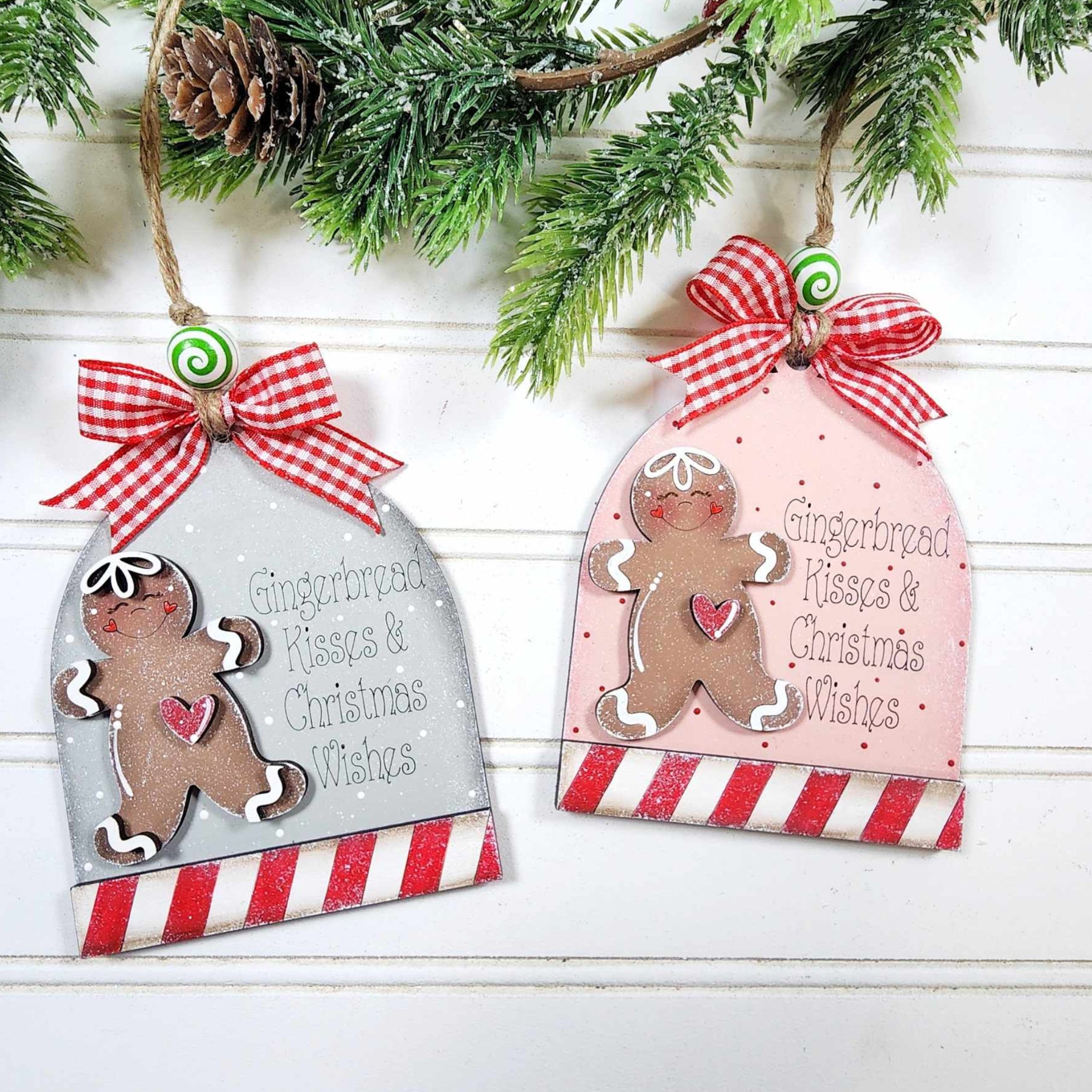 Two Christmas ornaments with gingerbread men designs hanging on a branch.