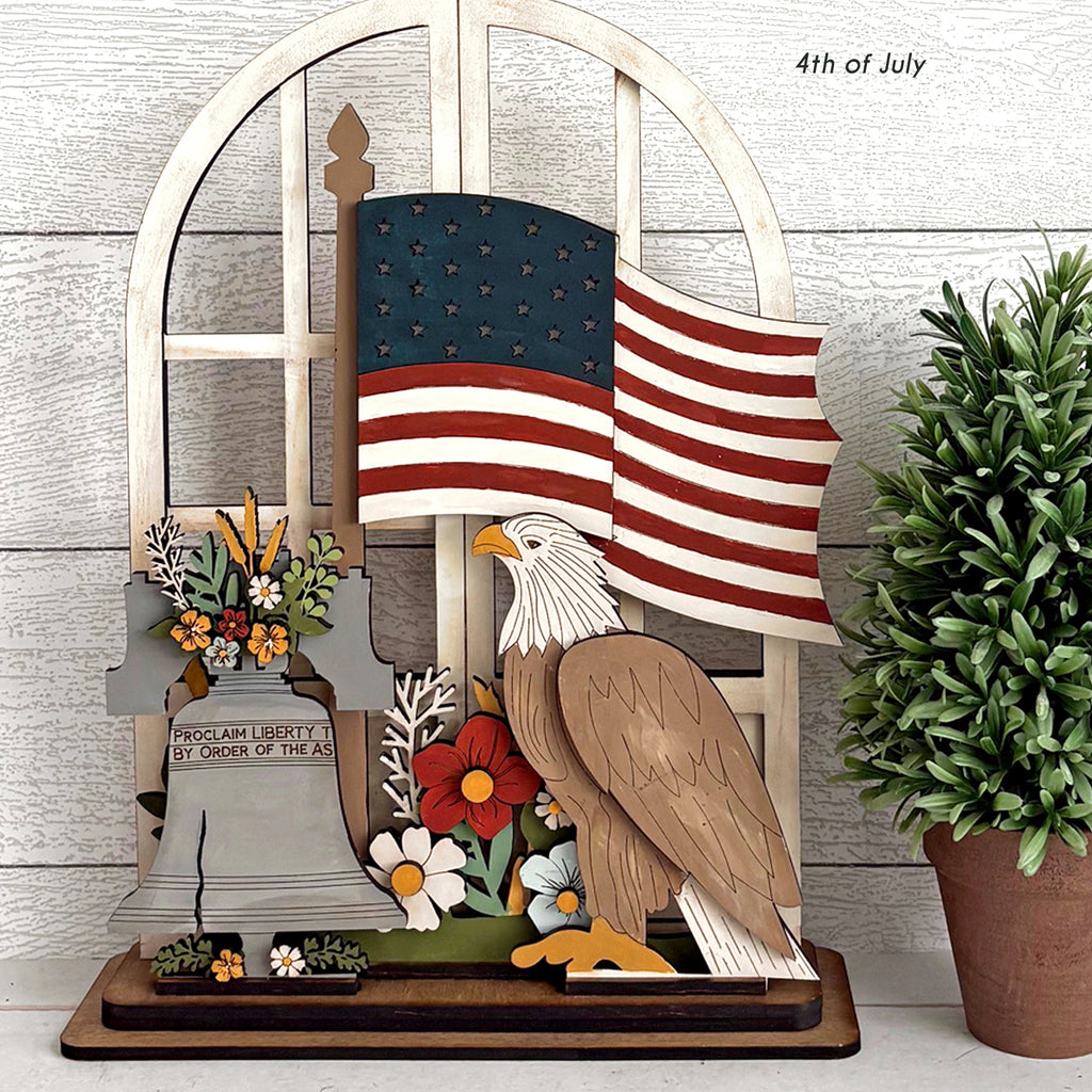 Decorative display with American flag, eagle, and flowers on a wooden stand.