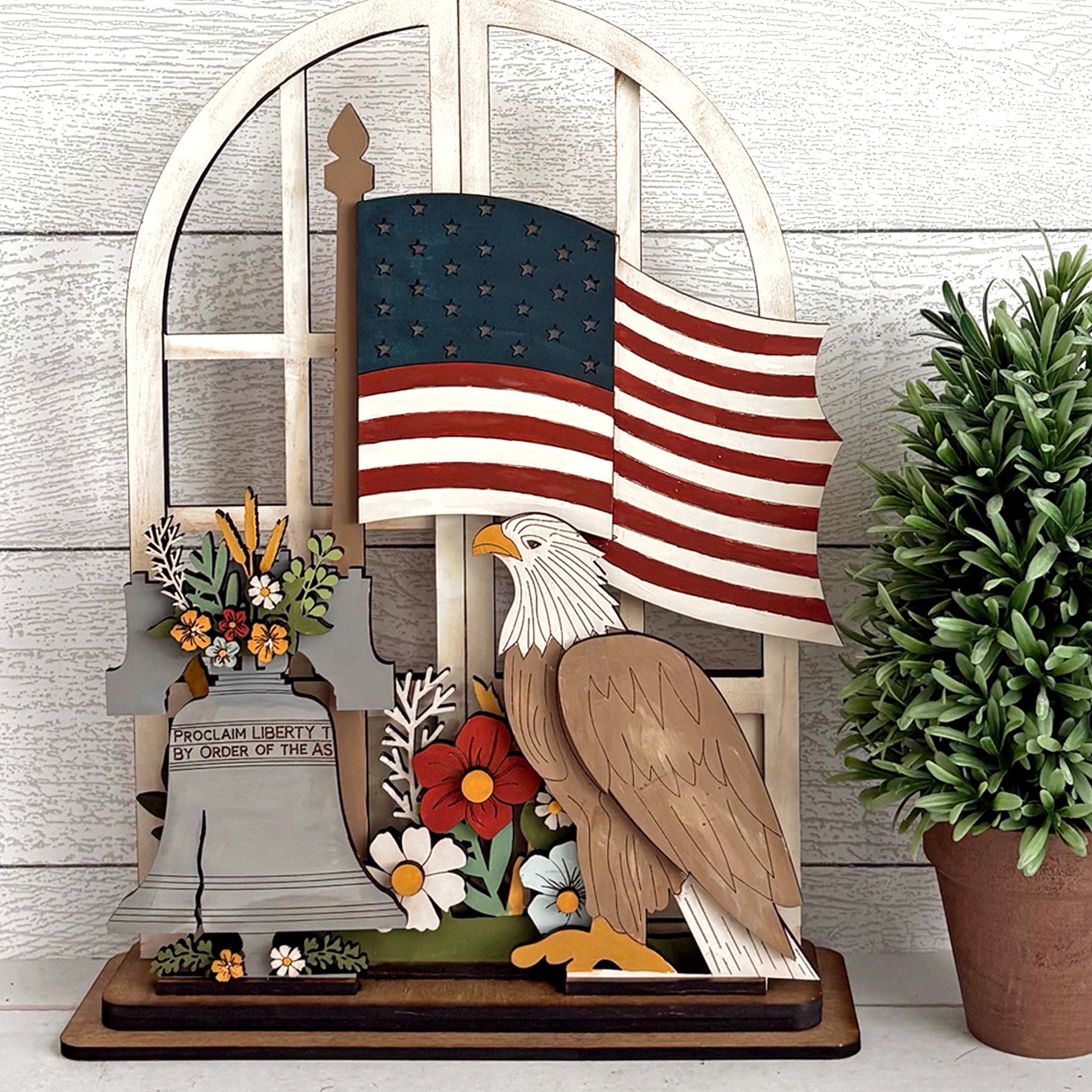 Decorative wooden sign with American flag, eagle, and flowers on a wooden stand.
