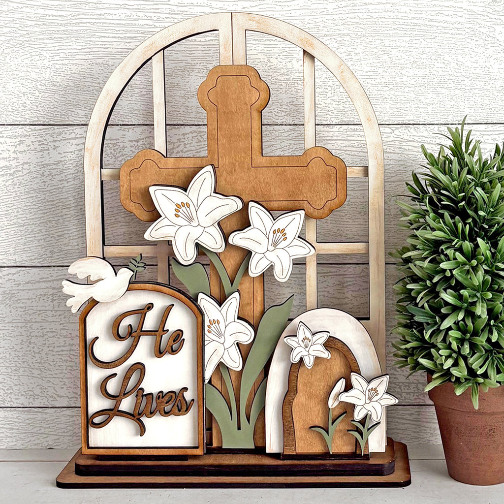 Wooden cross with lilies and 'He Lives' sign on a wooden background