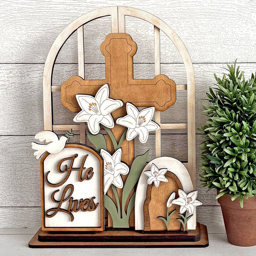 Wooden cross with lilies and 'He Lives' sign on a wooden background