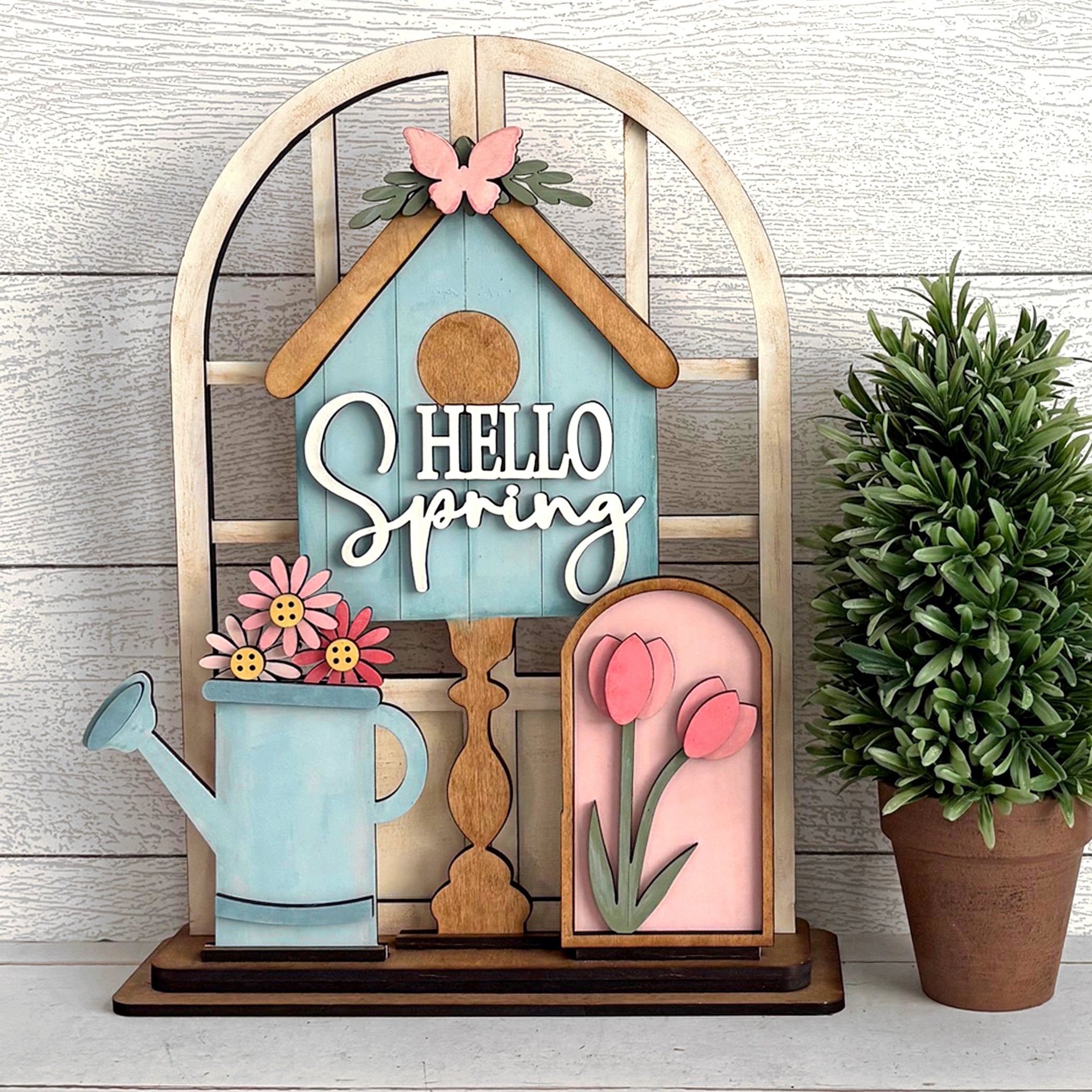 Decorative sign with 'Hello Spring' text, flowers, and a butterfly on a wooden background.