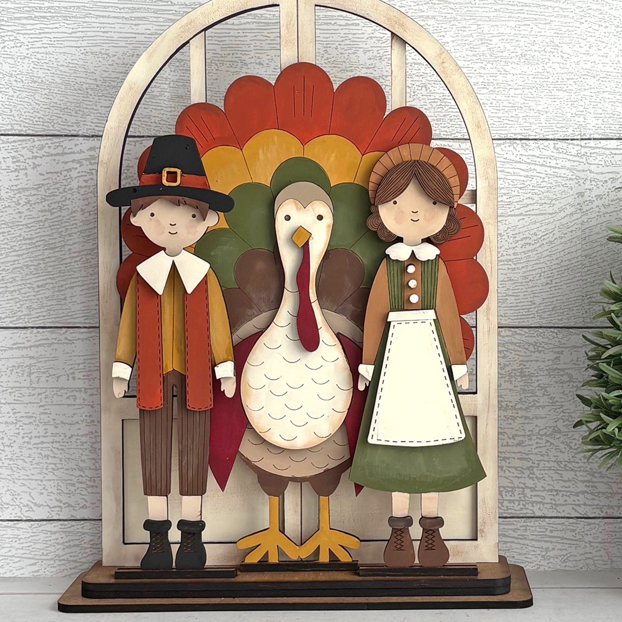 Decorative display with a boy, girl, and turkey against a wooden arch with autumn leaves.