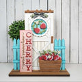 Decorative set with cherry-themed elements including a door, basket, and sign on a white wooden background.
